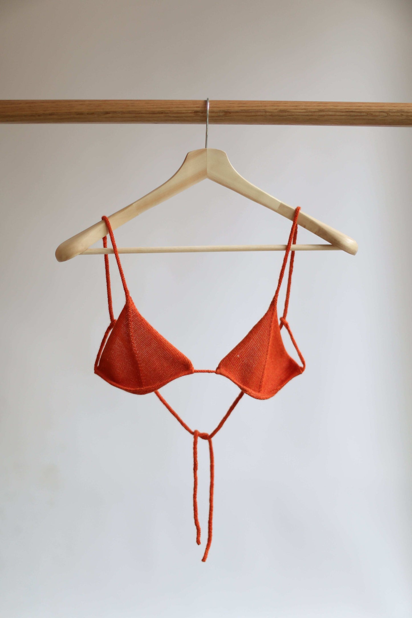 Orange knit bikini top on a hanger against a plain background