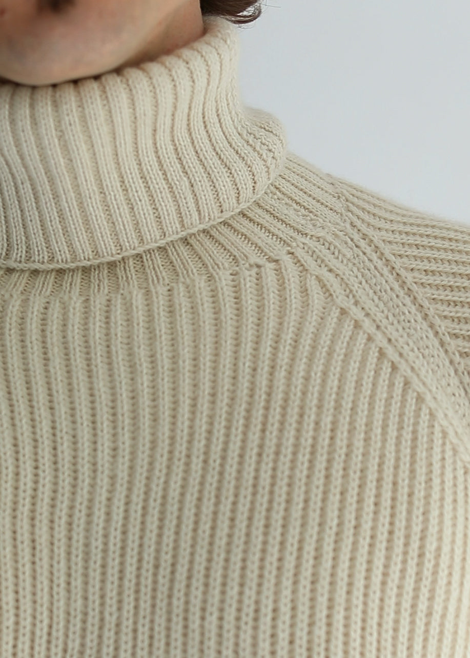 Collar detail of a white unisex turtleneck sweater made of baby alpaca wool with a fisherman rib design and worn by a man