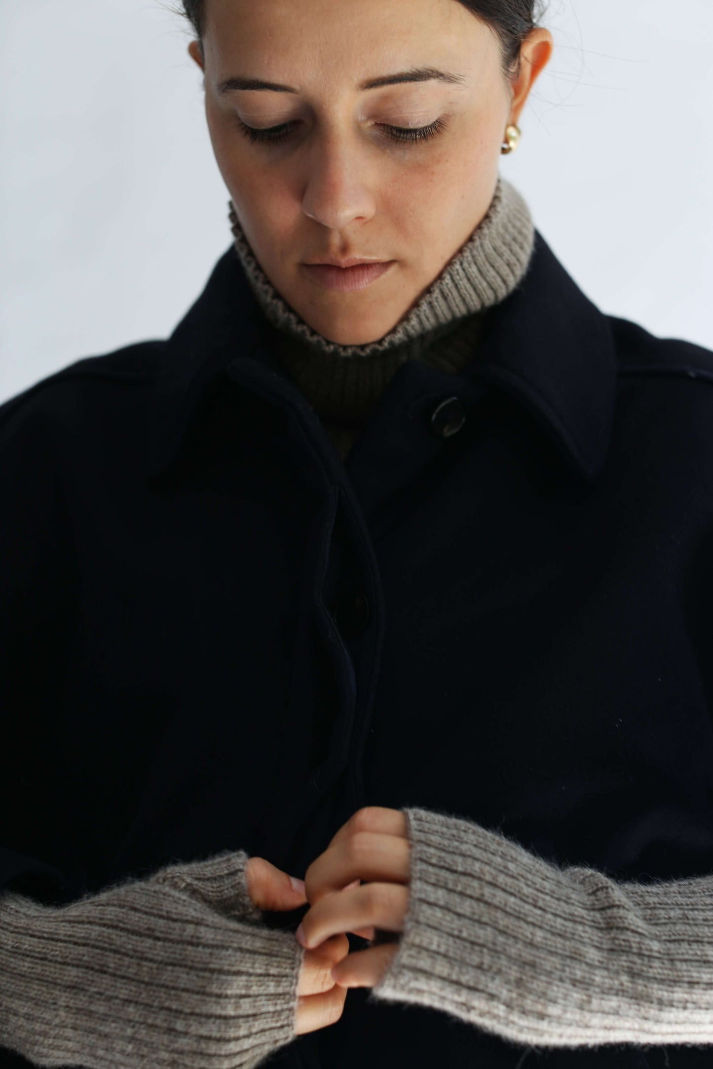 Close-up of a person wearing taupe alpaca knitted hand warmer sets against a plain white background.