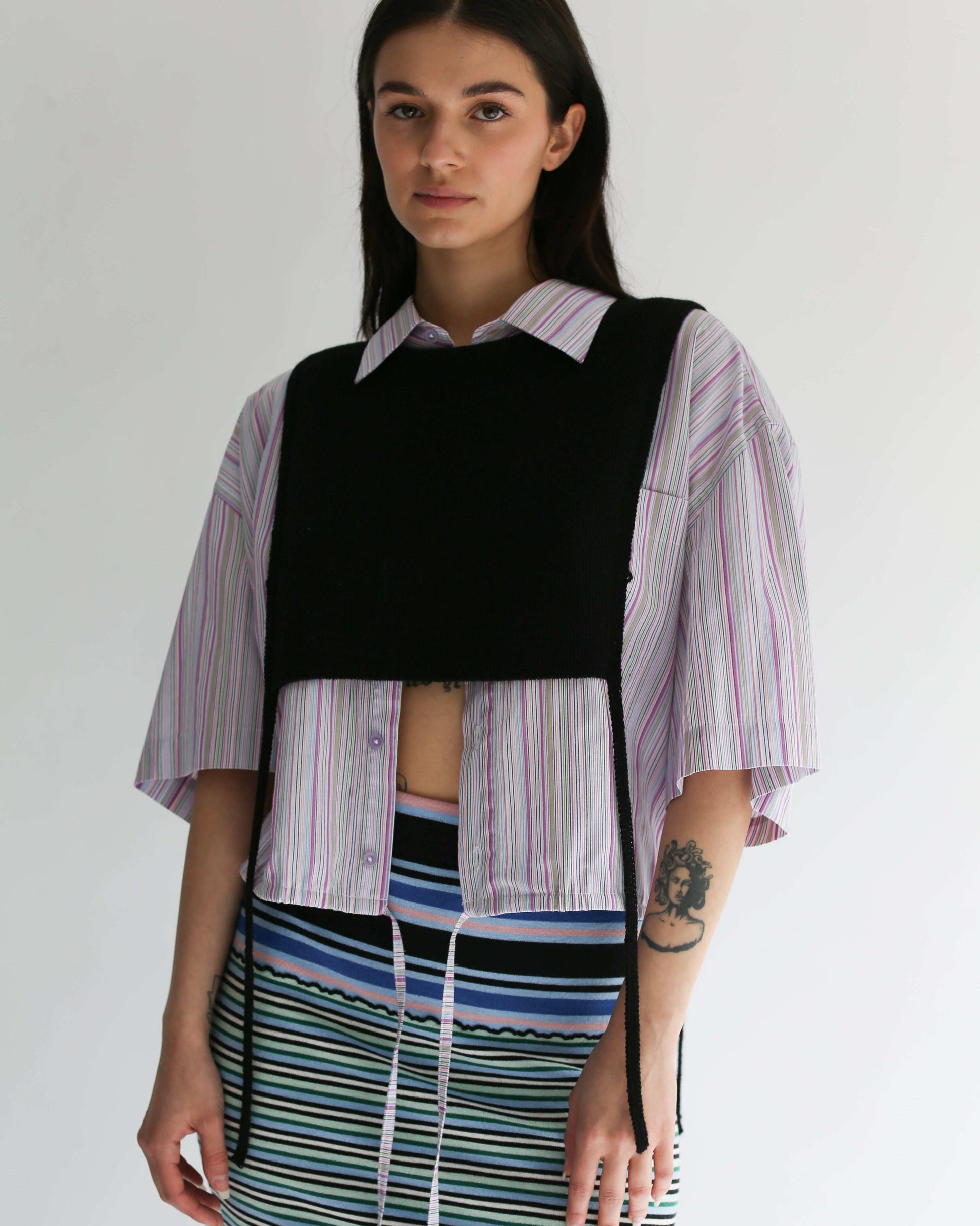 A woman wearing a black knit apron top with a striped shirt and striped skirt