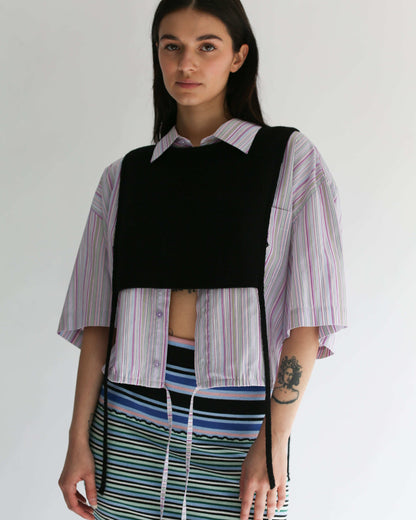 A woman wearing a black knit apron top with a striped shirt and striped skirt