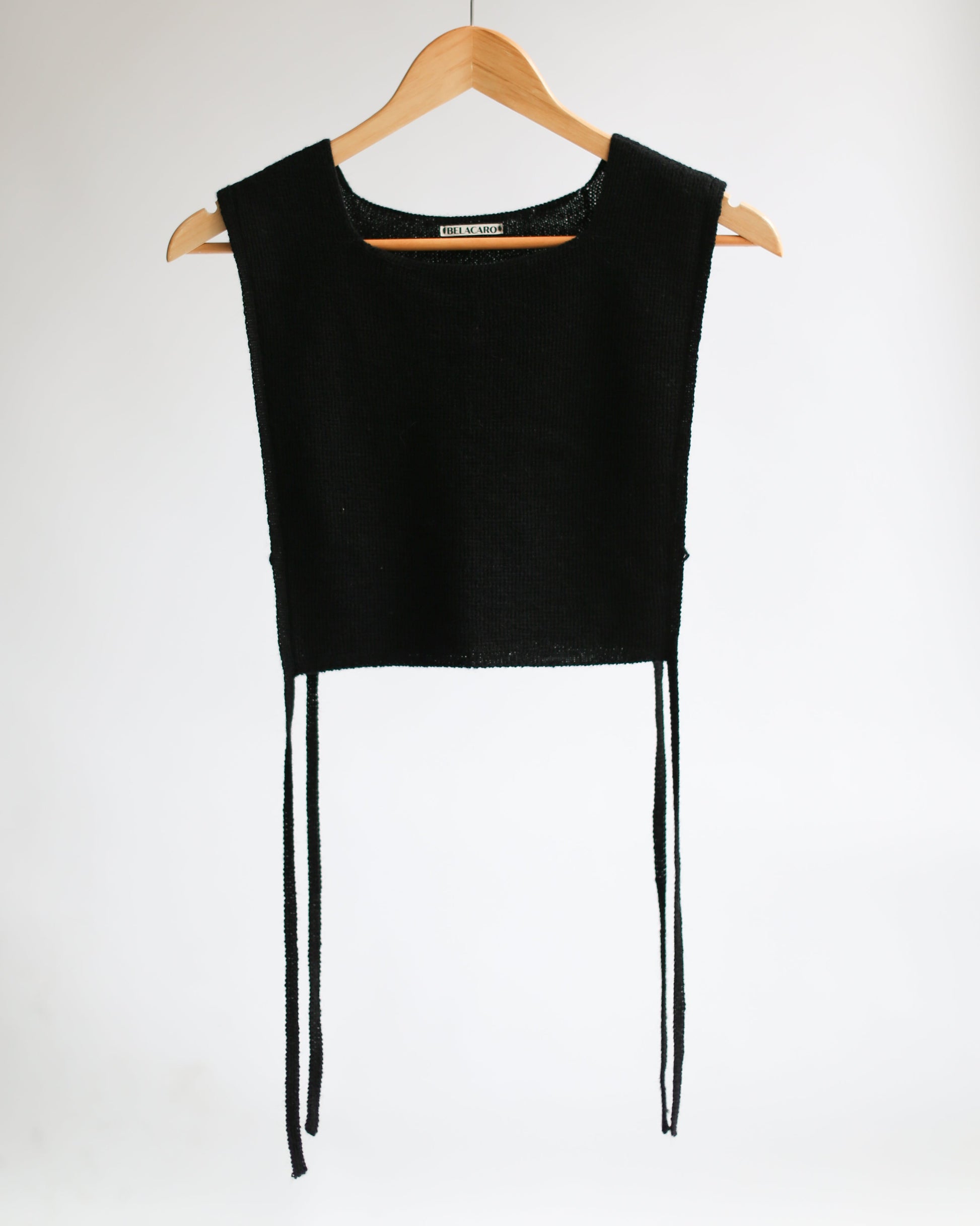 Black sleeveless apron top on a wooden hanger against a white background