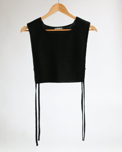 Black sleeveless apron top on a wooden hanger against a white background