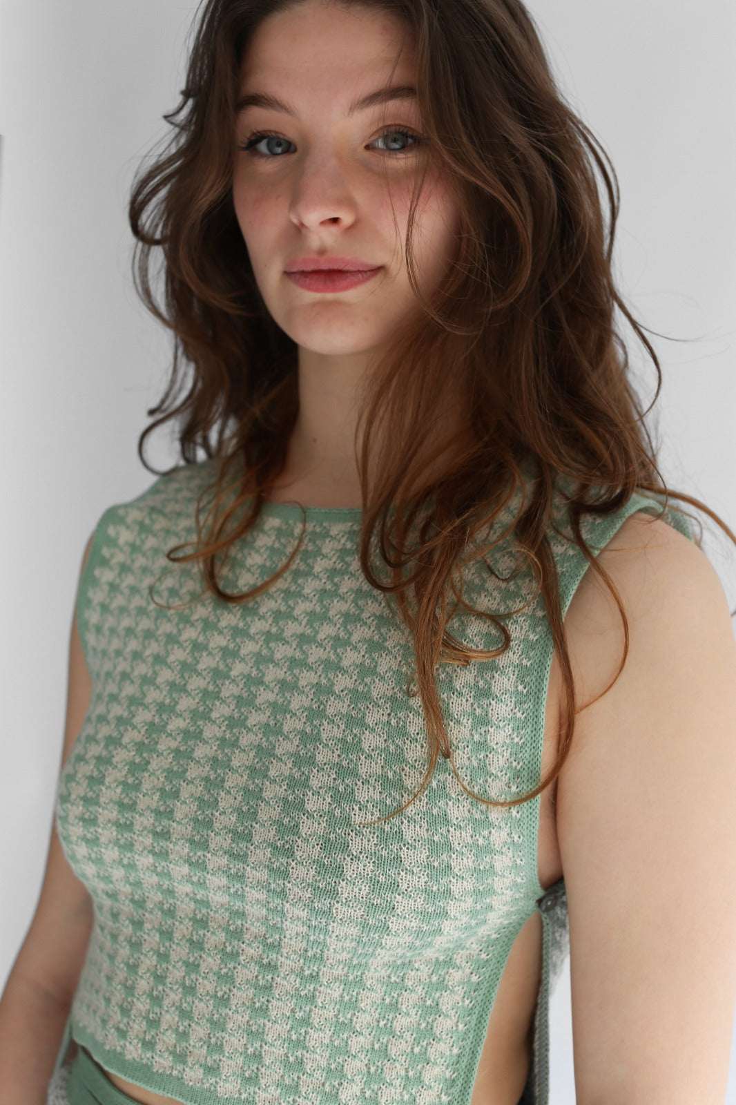 Woman wearing a green knitted patterned top against a plain background