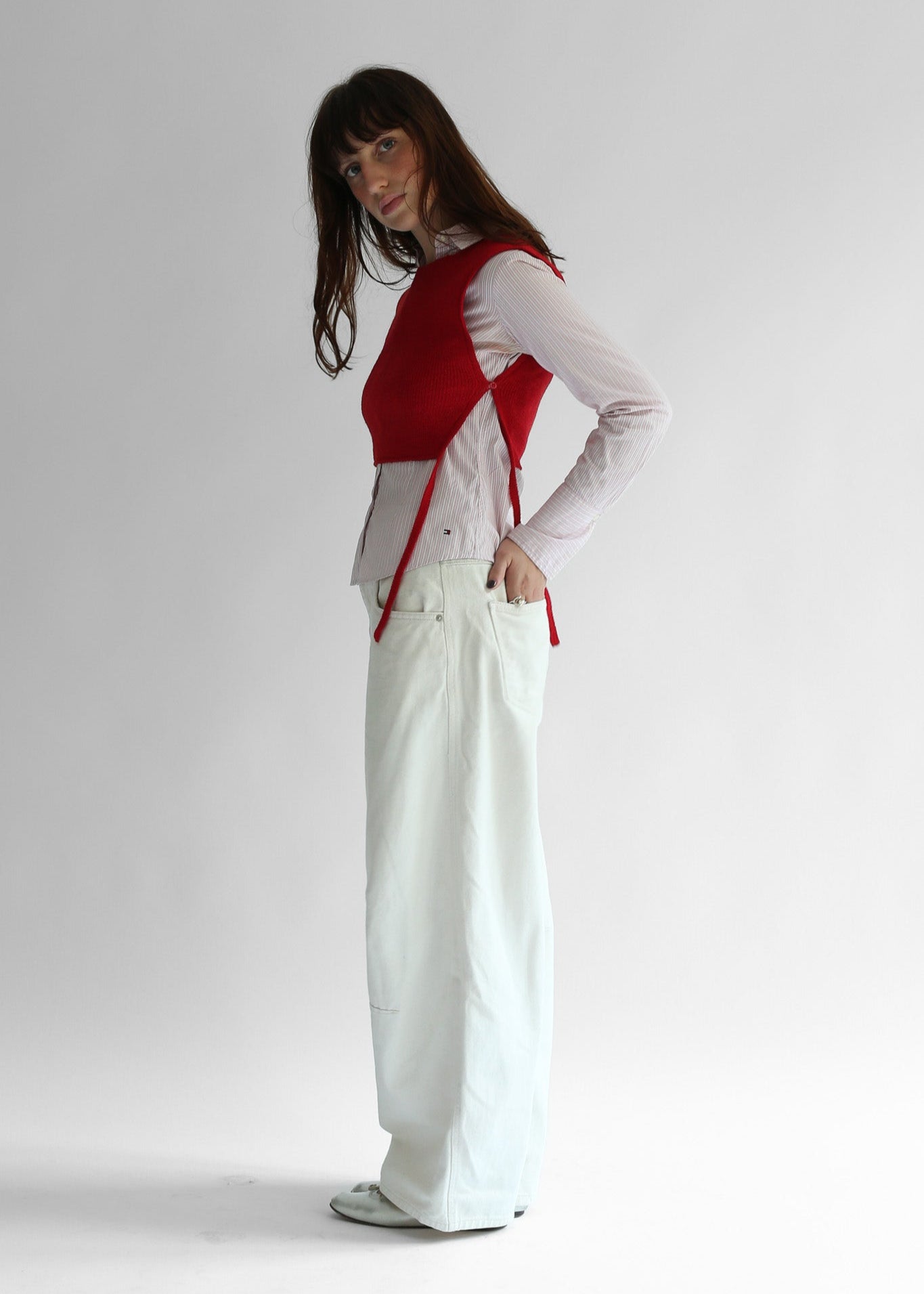 A woman wearing a red knit apron with white pants on a plain background