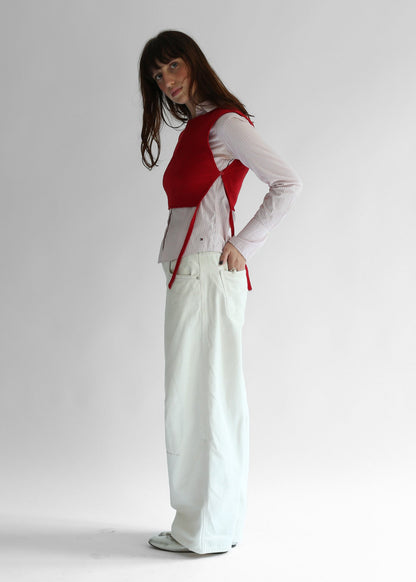 A woman wearing a red knit apron with white pants on a plain background