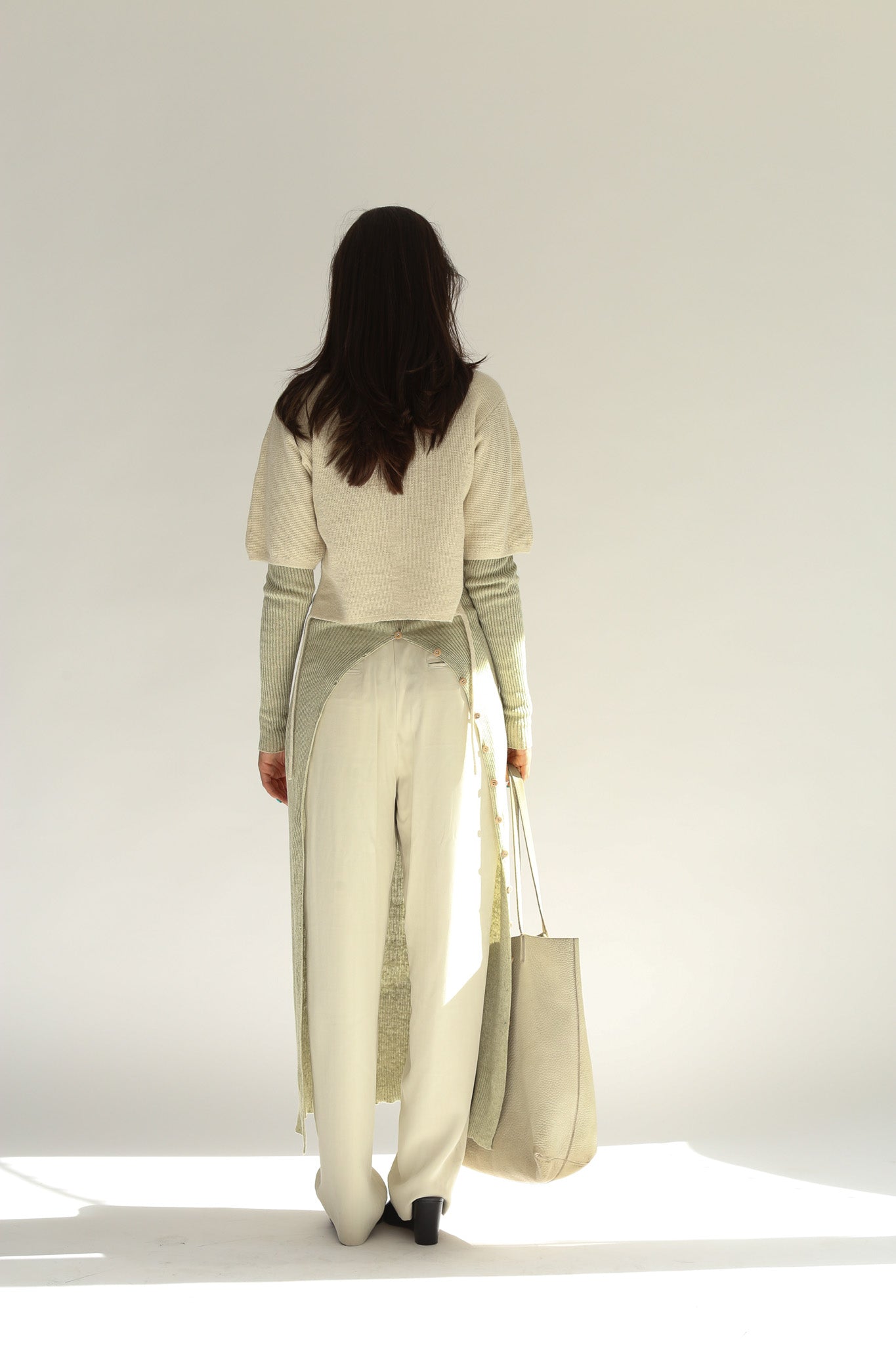 Back view of the model wearing the belacaro apron with sleeves knit, showcasing the open-back layered style and relaxed fit.