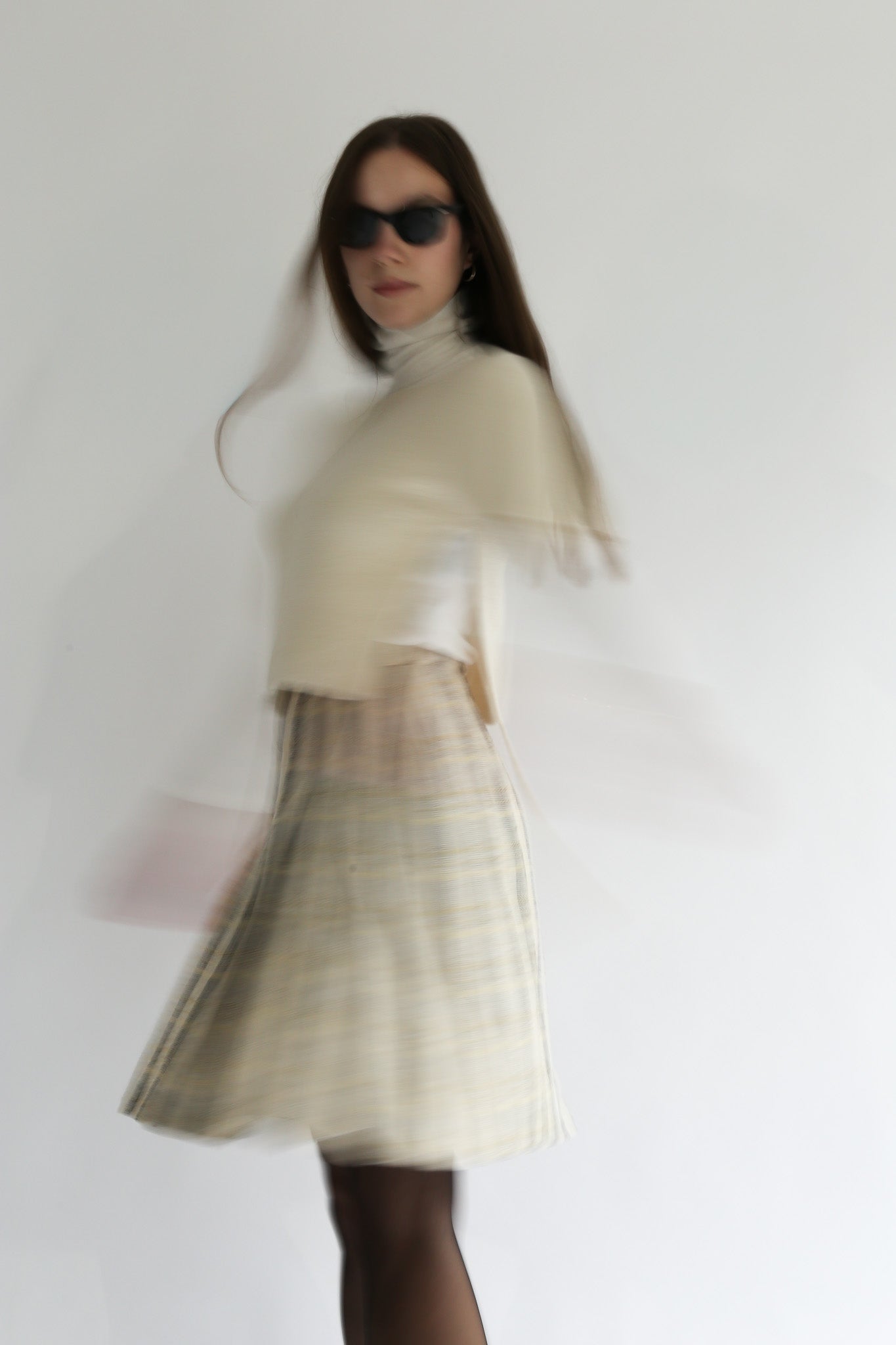 Model wearing the belacaro beige apron with sleeves knit in baby alpaca, captured in motion to highlight its light texture and fluid silhouette