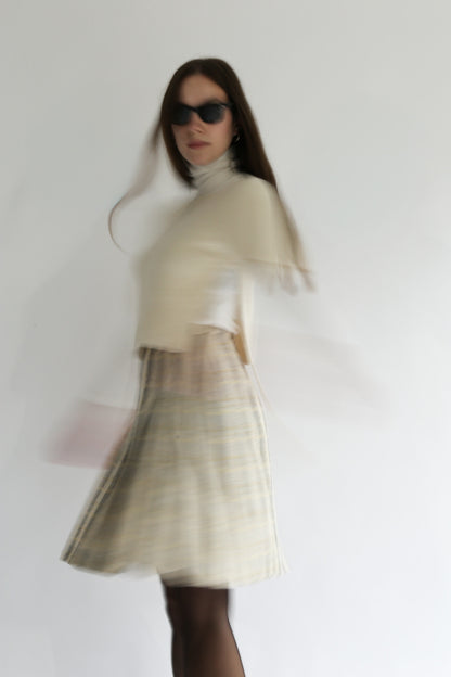 Model wearing the belacaro beige apron with sleeves knit in baby alpaca, captured in motion to highlight its light texture and fluid silhouette