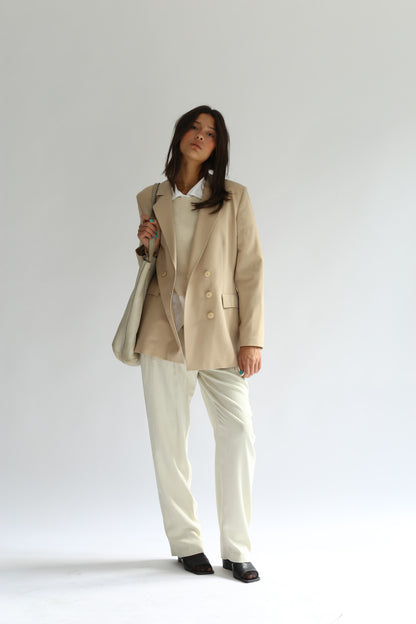 Model wearing the belacaro apron with sleeves knit layered over a white shirt and beige blazer, styled with cream trousers and black sandals.