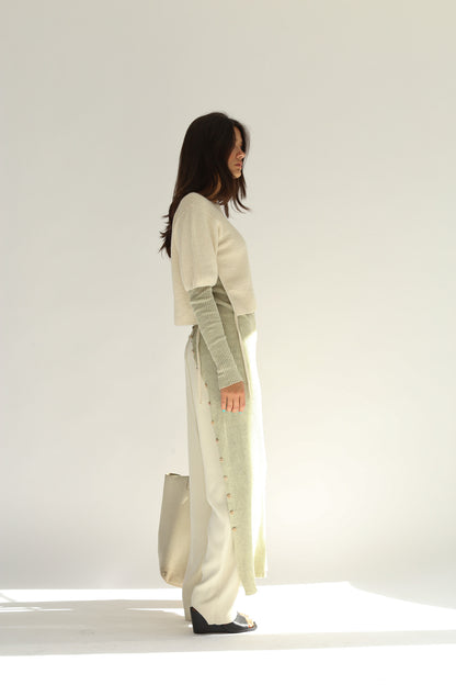 Side view of the belacaro apron with sleeves knit in baby alpaca layered over light trousers, showing the drawcord detail and buttoned slit.