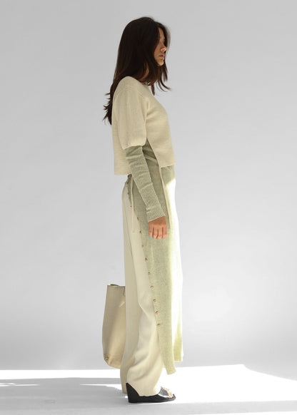 Side view of the belacaro apron with sleeves knit in baby alpaca layered over light trousers, showing the drawcord detail and buttoned slit.