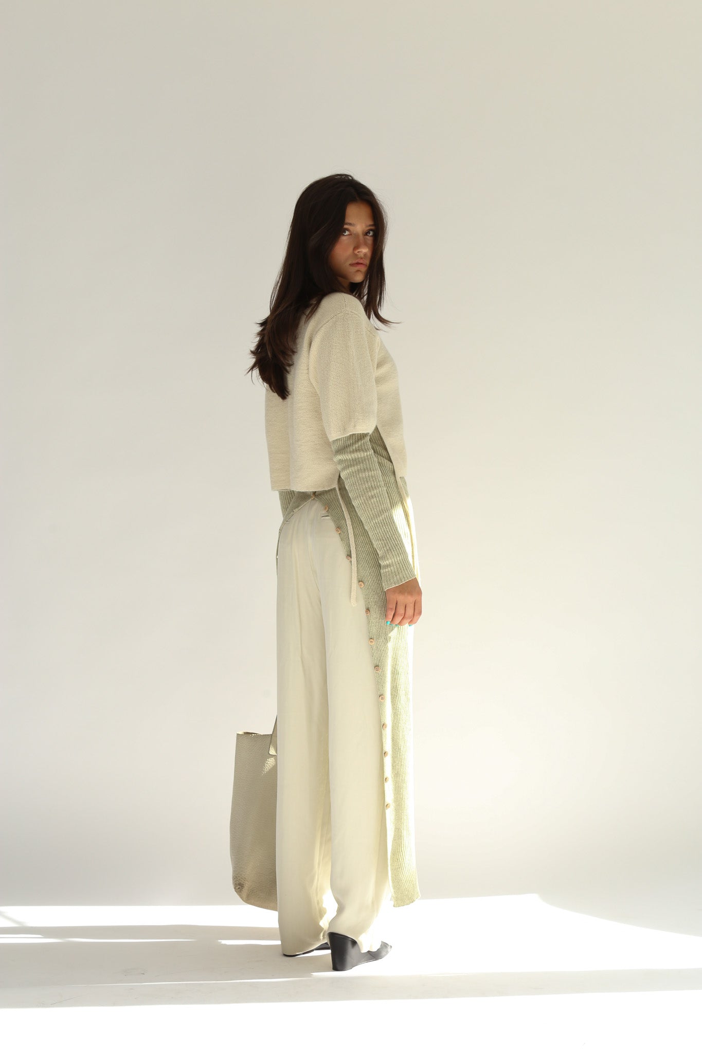 Three quarter rear view of the belacaro apron with sleeves knit in baby alpaca layered over light trousers, showing the drawcord detail and buttoned slit.