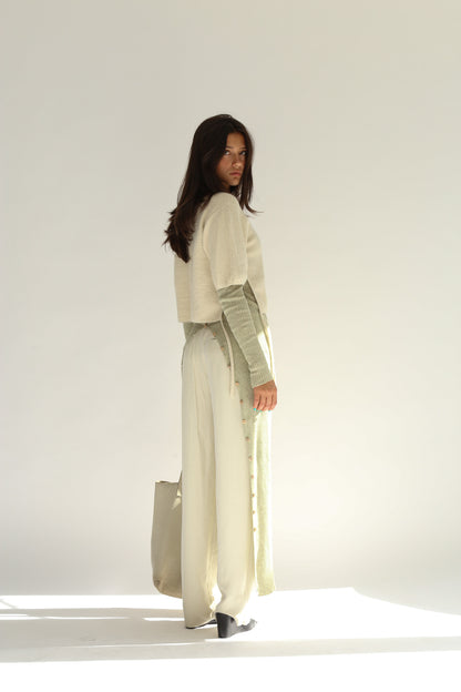 Three quarter rear view of the belacaro apron with sleeves knit in baby alpaca layered over light trousers, showing the drawcord detail and buttoned slit.