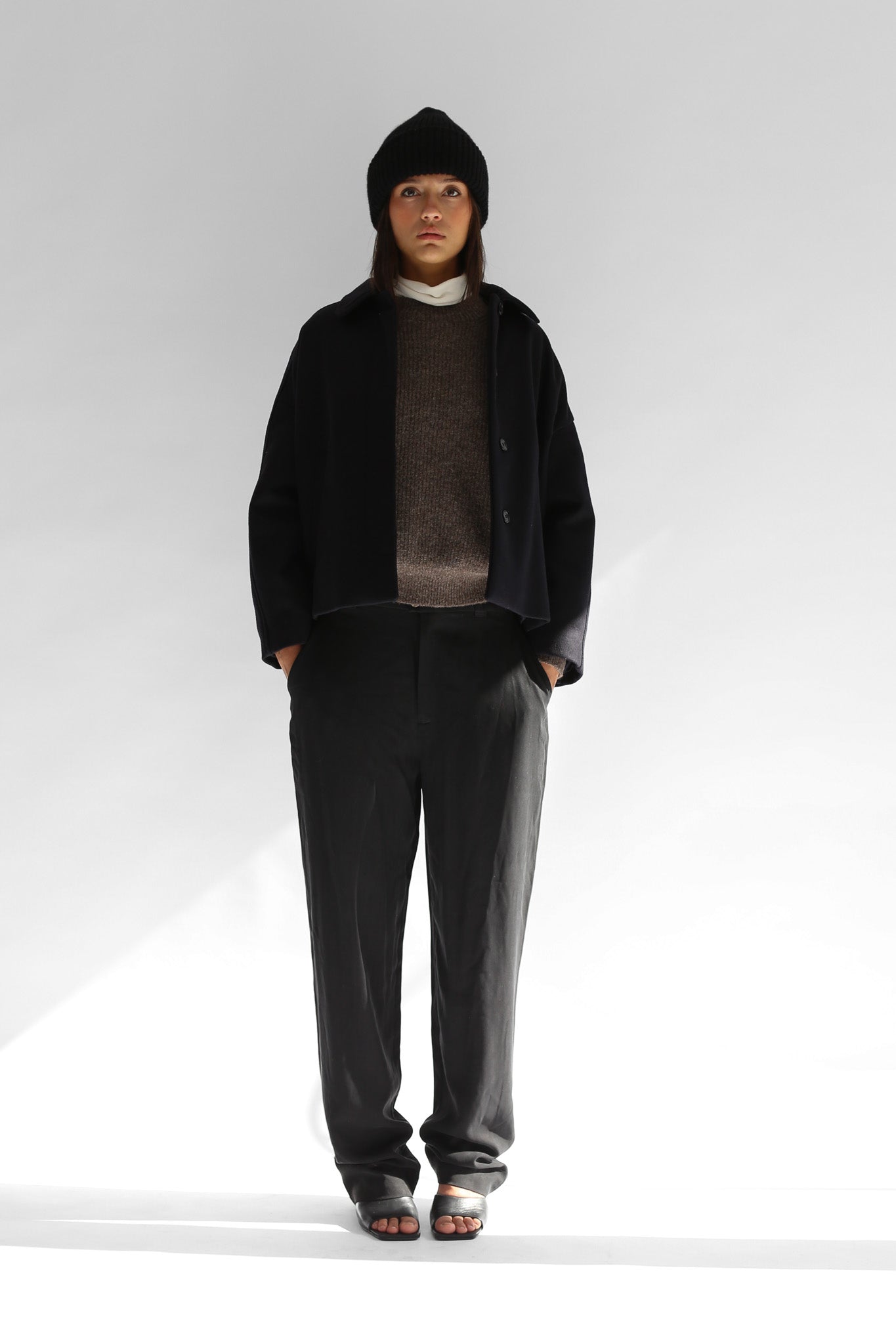 Belacaro beanie in black baby alpaca, ribbed knit with folded brim, worn by model with dark outerwear, full body shot