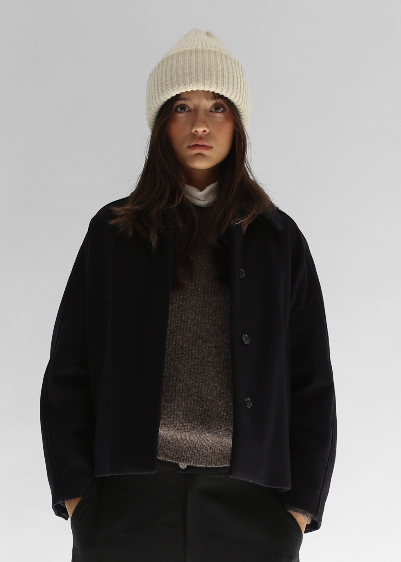 Belacaro beanie in black baby alpaca, ribbed knit with folded brim, worn by model with dark outerwear, close-up portrait.