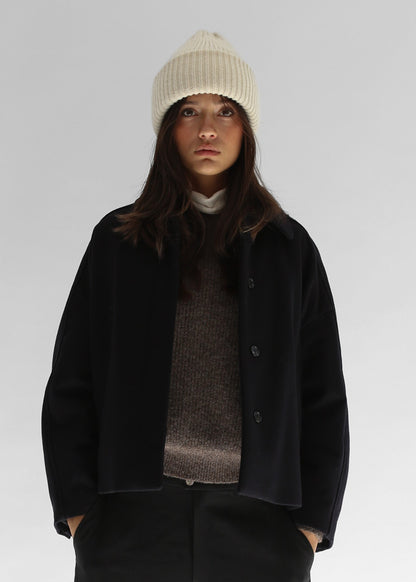 Belacaro beanie in black baby alpaca, ribbed knit with folded brim, worn by model with dark outerwear, close-up portrait.