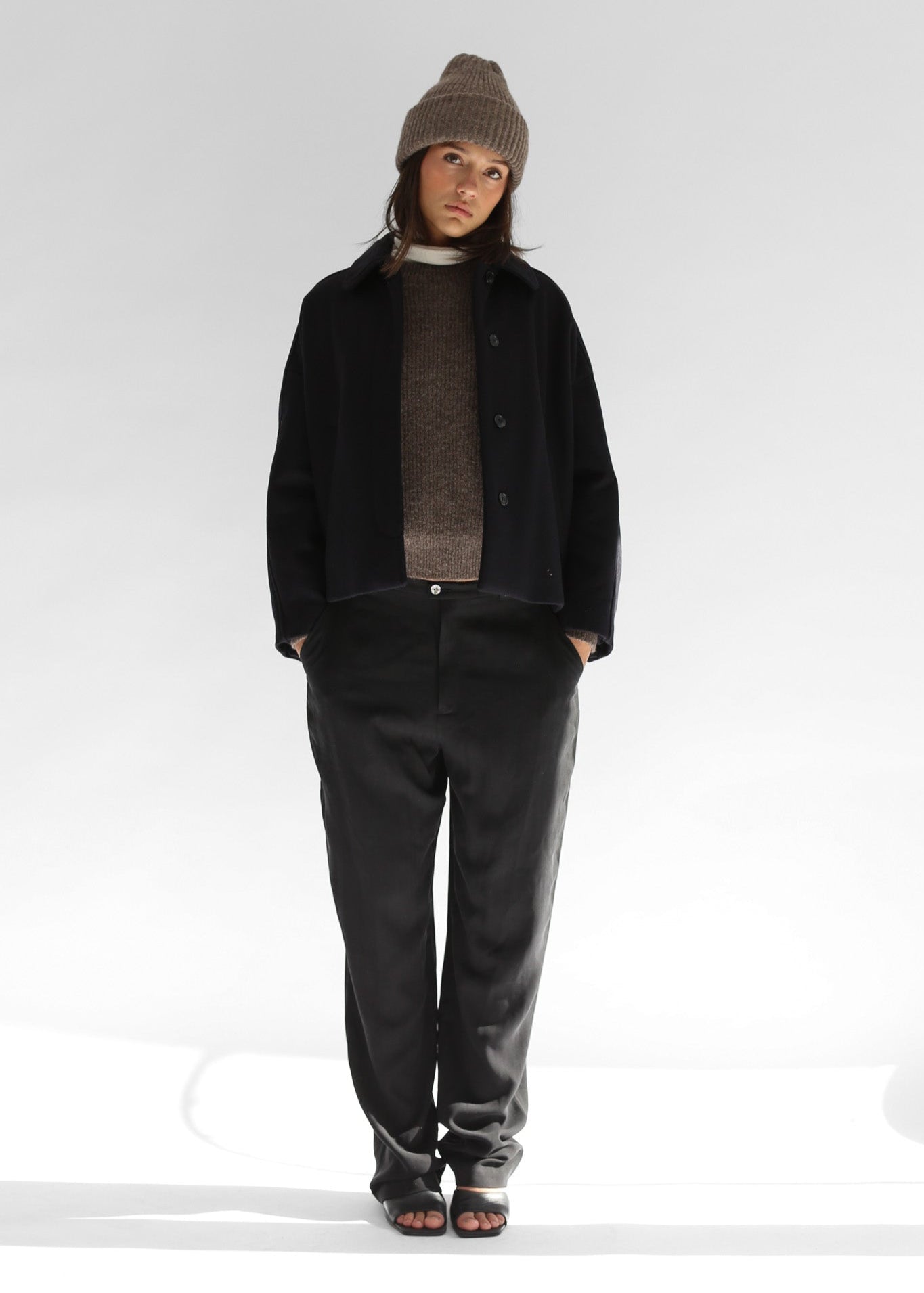 Model wearing the Belacaro kids beanie in grey baby alpaca, styled with a black wool short jacket and baggy grey pants, front view.