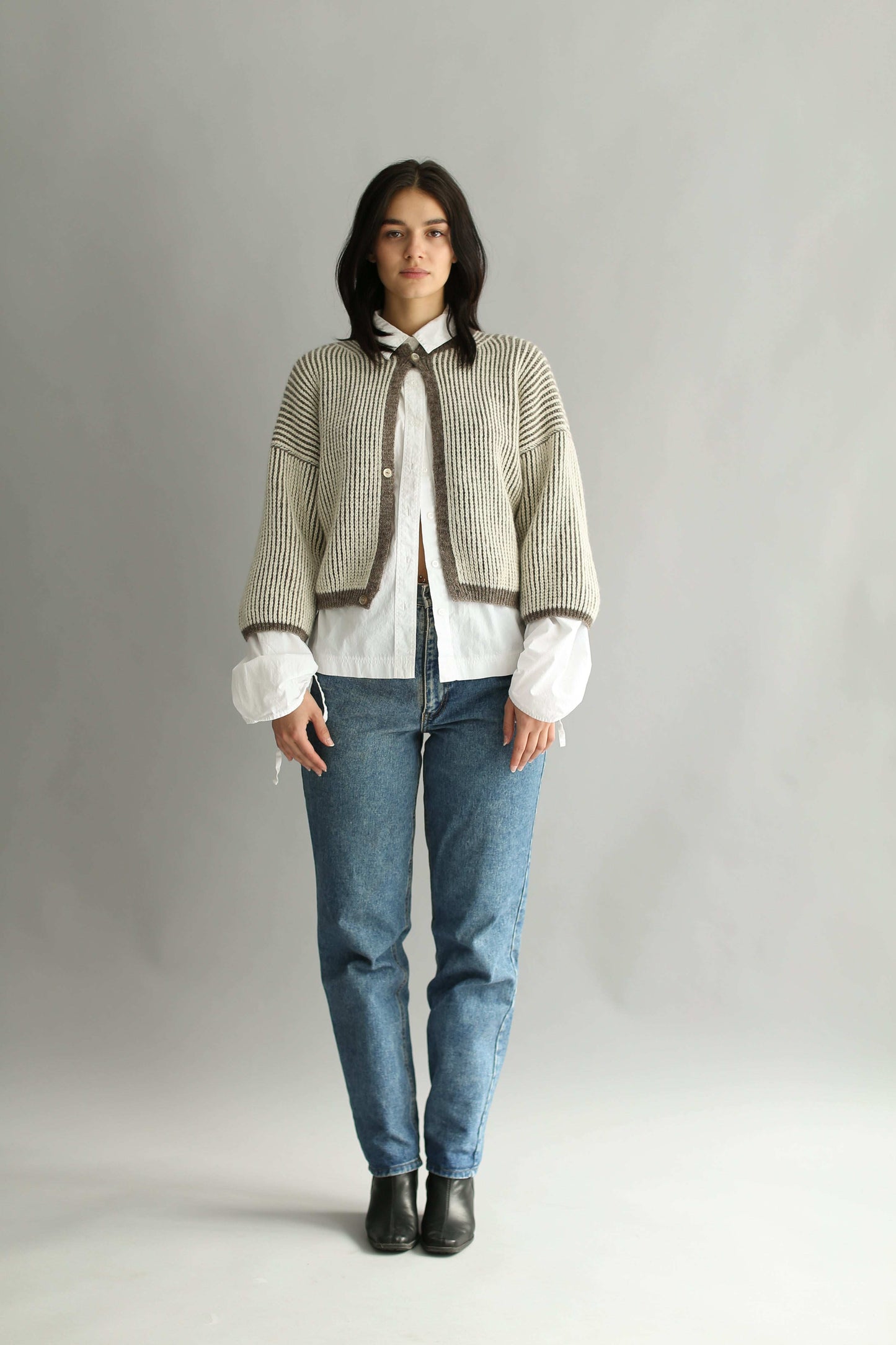 Model wearing a knitted brown and white bicolor cardigan and denim blue jeans on a plain background