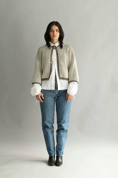 Model wearing a knitted brown and white bicolor cardigan and denim blue jeans on a plain background