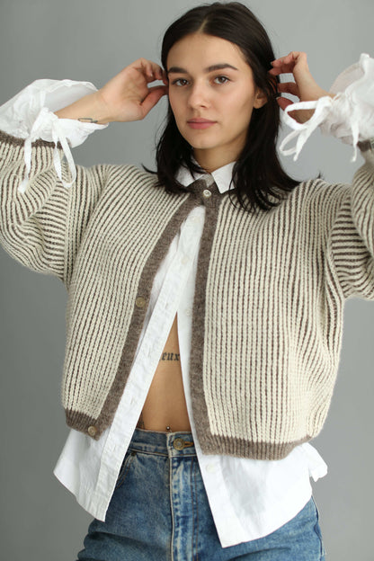 Model wearing a knitted brown and white bicolor cardigan and denim blue jeans on a plain background