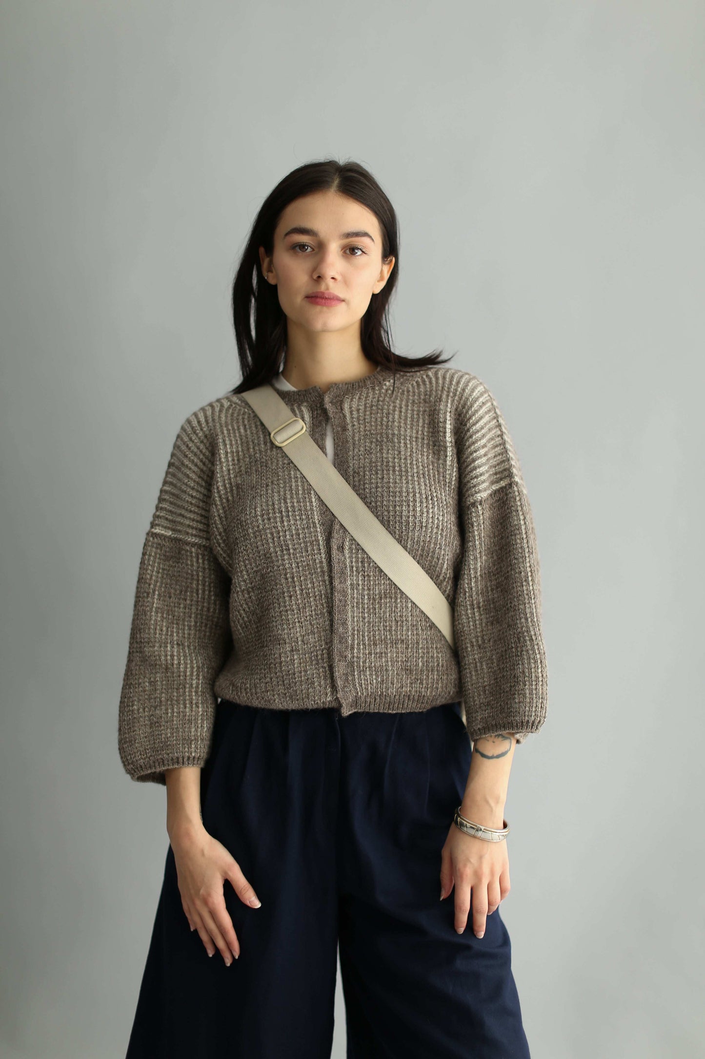 Model wearing a knitted brown and white bicolor cardigan and navy pants on a plain background