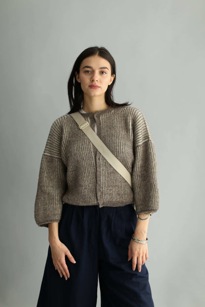 Model wearing a knitted brown and white bicolor cardigan and navy pants on a plain background