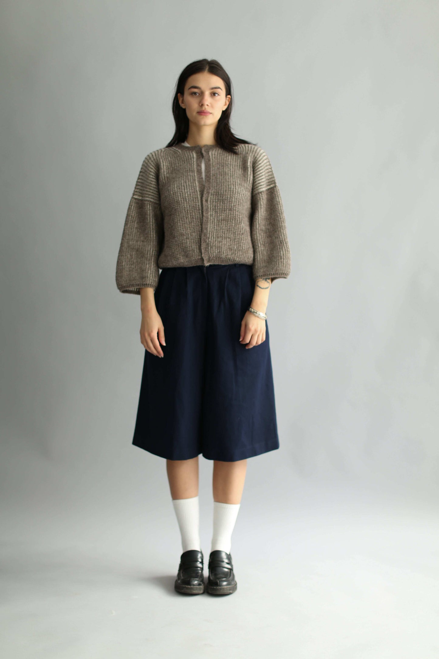 Model wearing a knitted brown and white bicolor cardigan and navy skirt on a plain background