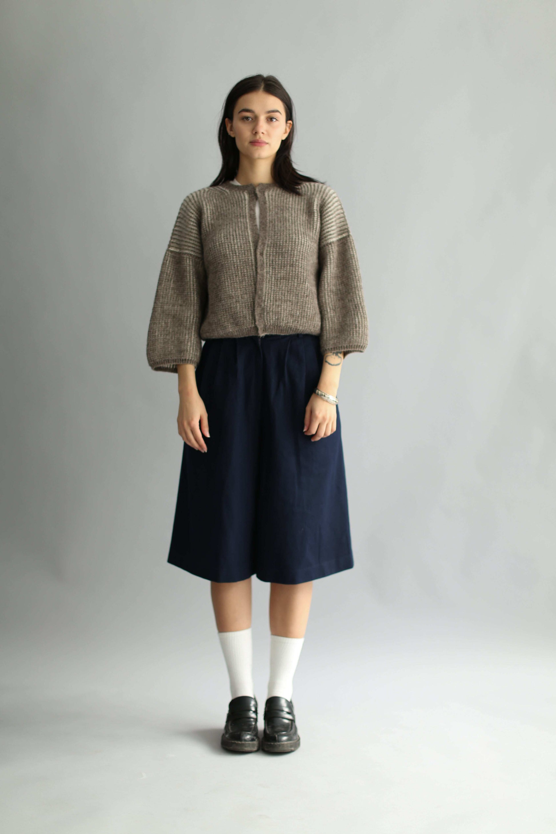 Model wearing a knitted brown and white bicolor cardigan and navy skirt on a plain background
