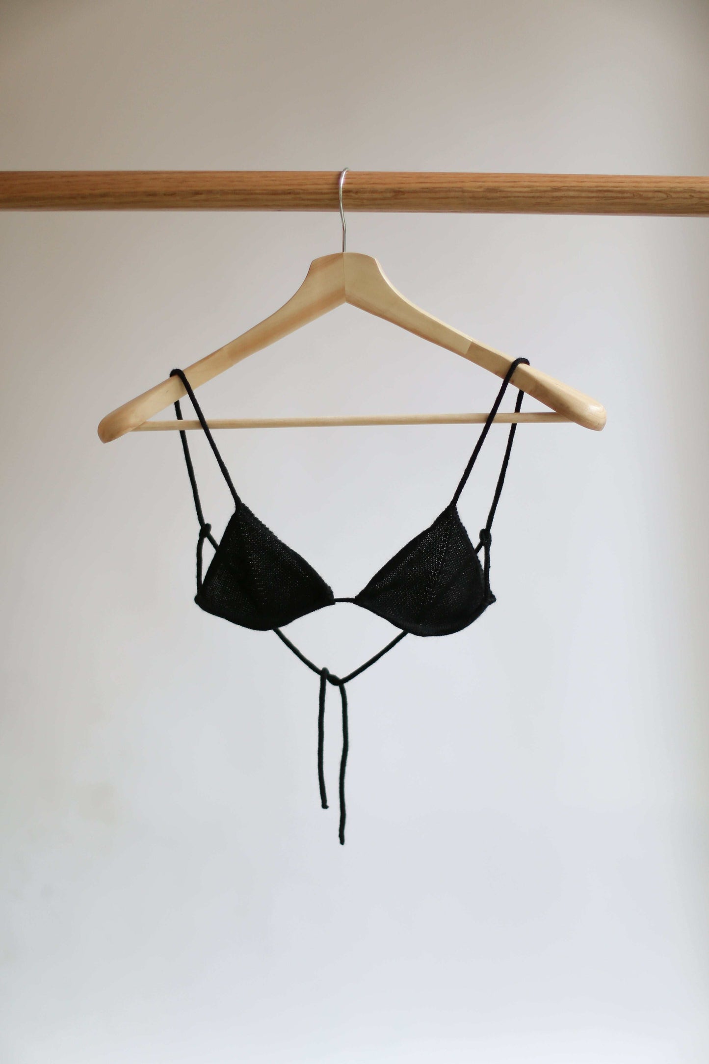 Black knit bikini top on a hanger against a plain background