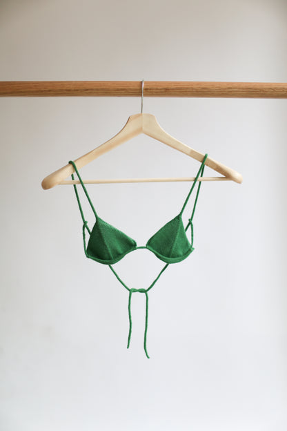 Green knit bikini top on a hanger against a plain background