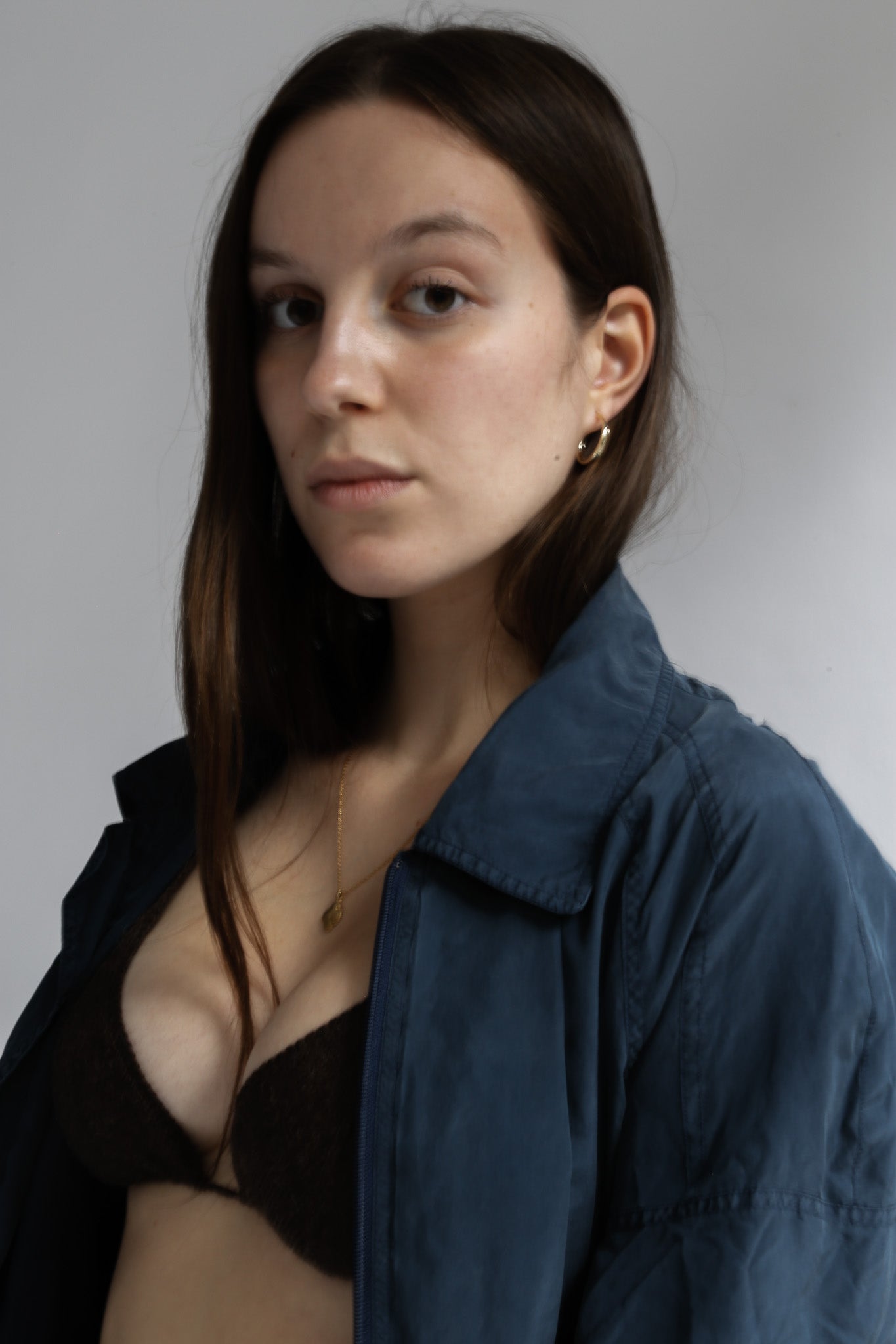 Woman wearing a dark jacket over a brown bralette on a plain background