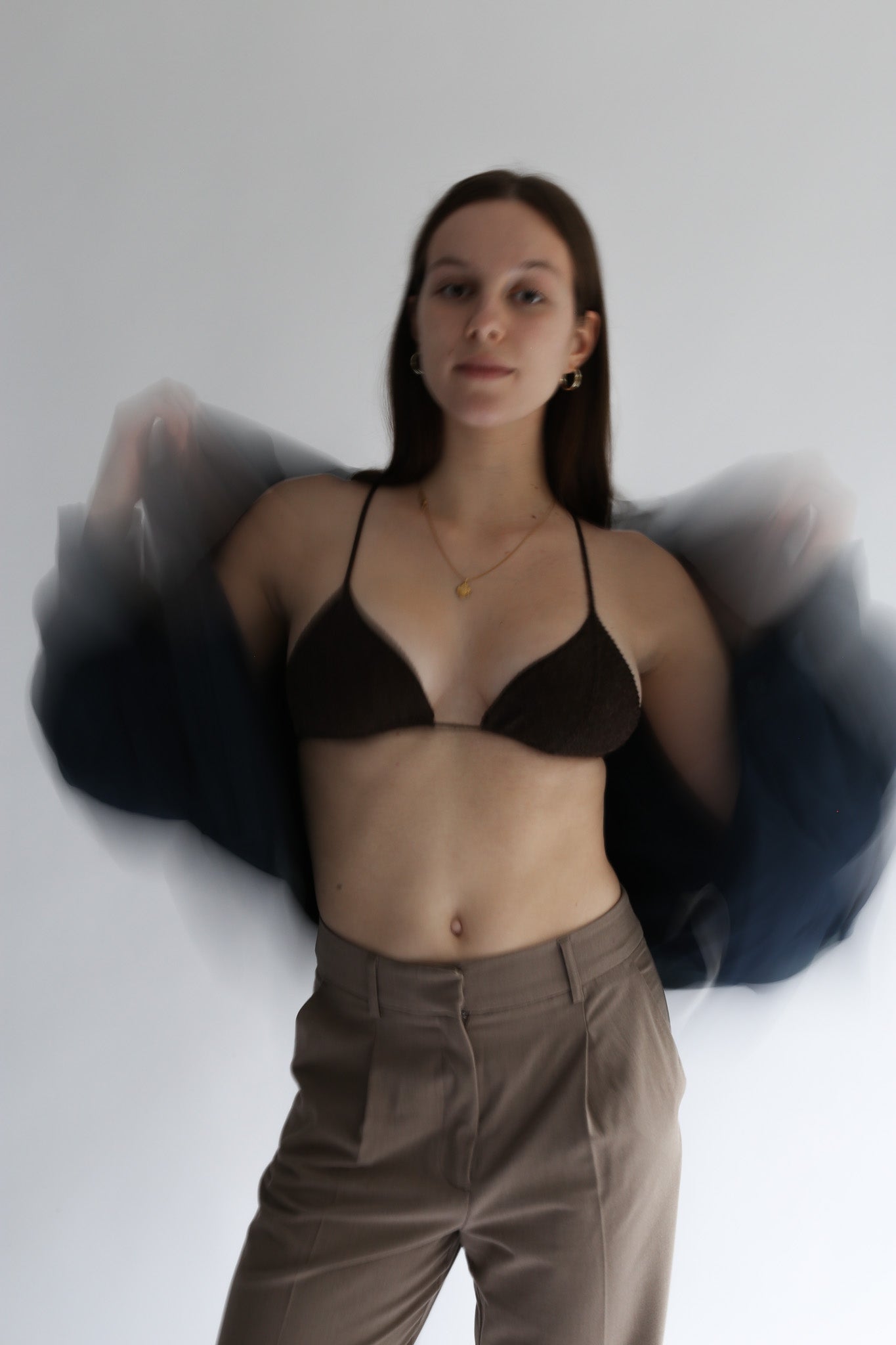 Woman wearing a black knit bra, bralette, and brown pants against a plain background