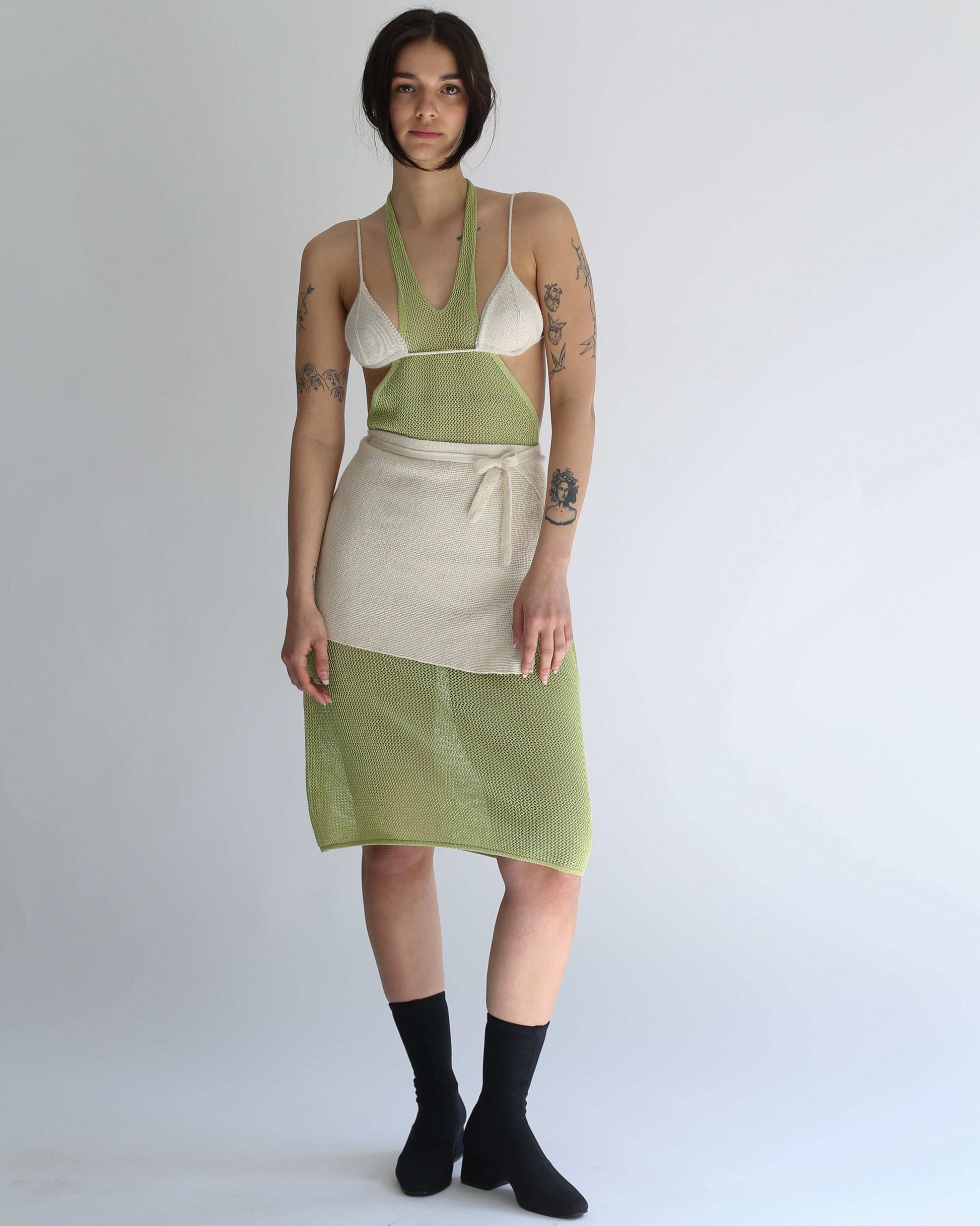 Woman wearing a green knit dress, white knit bikini and white knit skirt