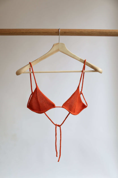 Orange knit bikini top on a hanger against a plain background