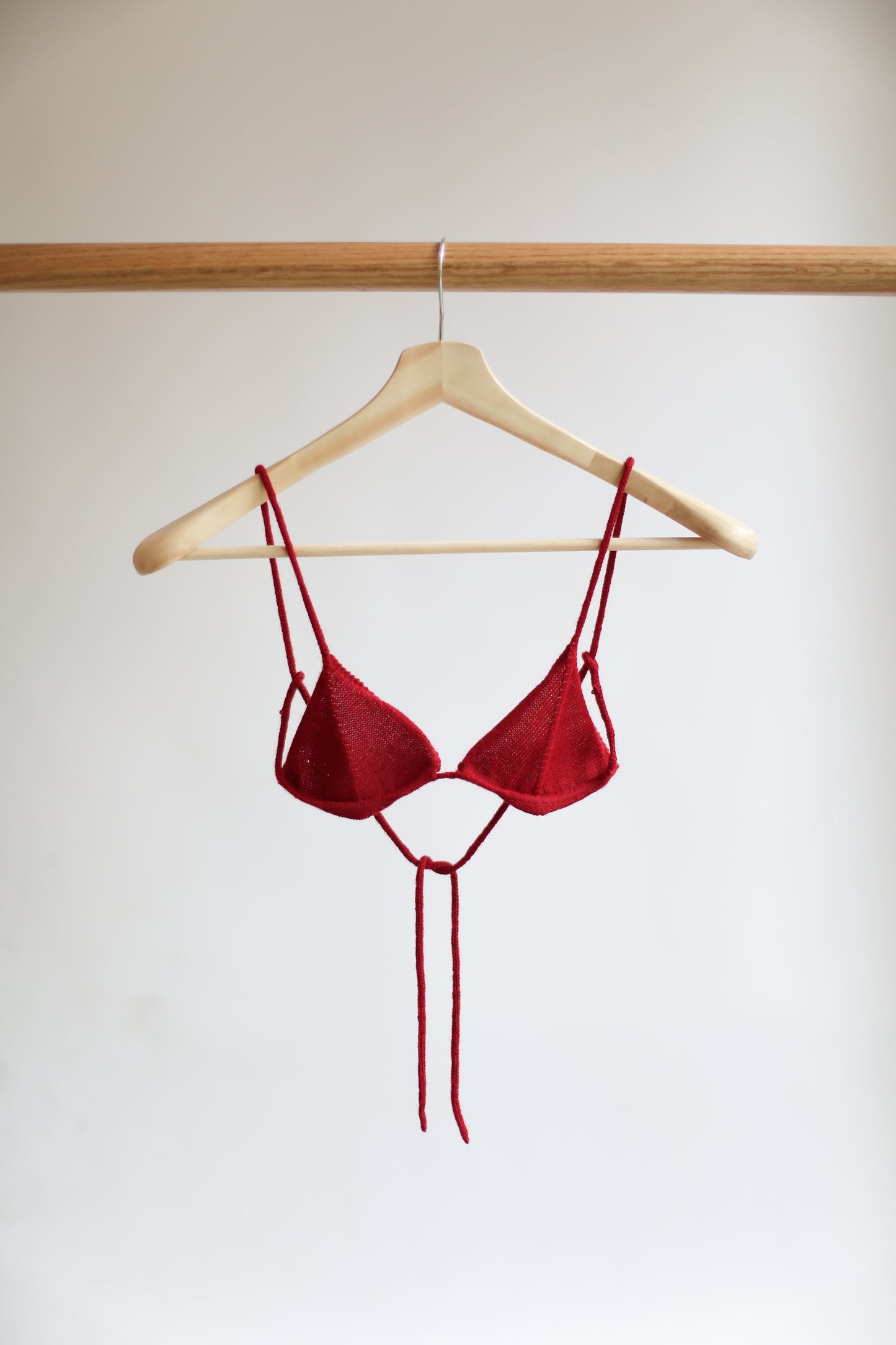 Red knit bikini top on a hanger against a plain background