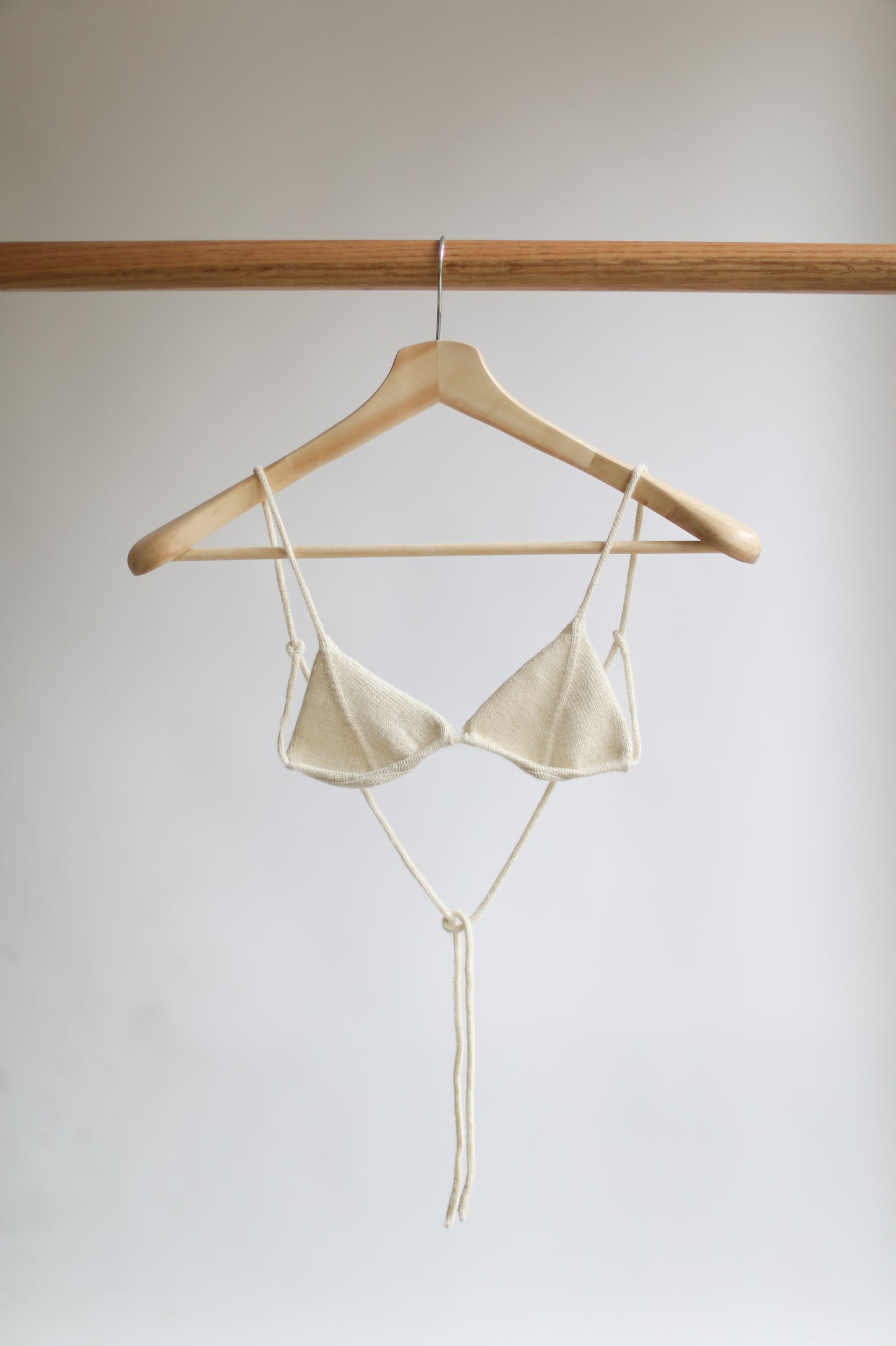 White knit bikini top on a hanger against a plain background