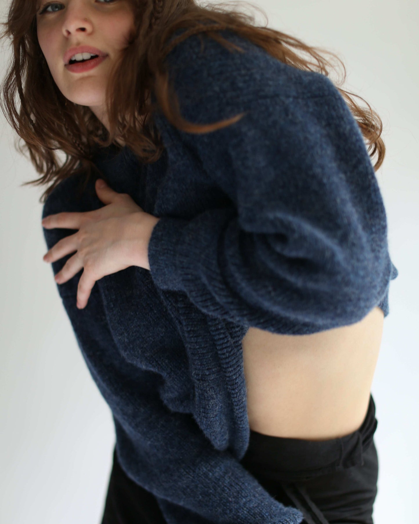A woman dancing and wearing a blue crewneck sweater on a plain background