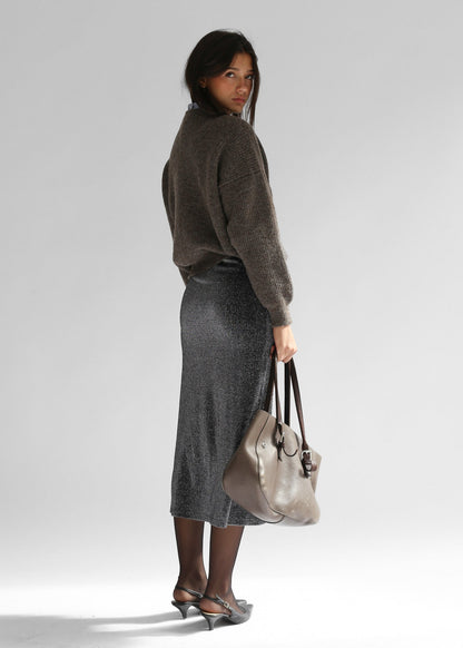 A woman wearing a brown crewneck sweater with a grey skirt on a plain background from the back
