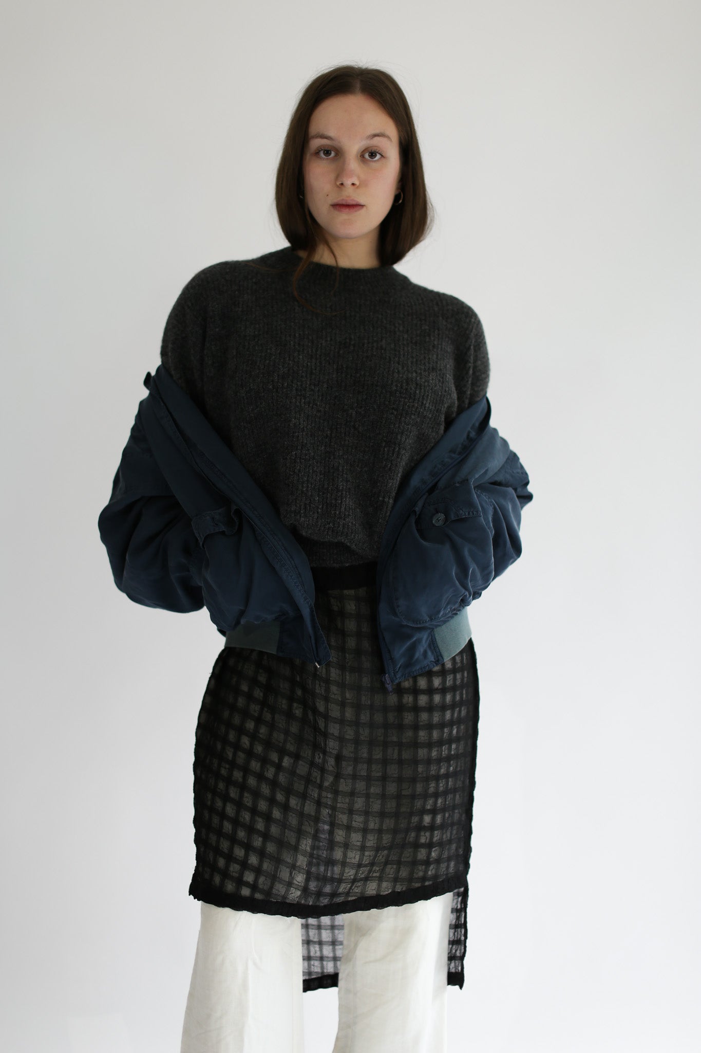 Woman wearing a grey sweater and plaid skirt with a blue jacket over shoulders on a white background