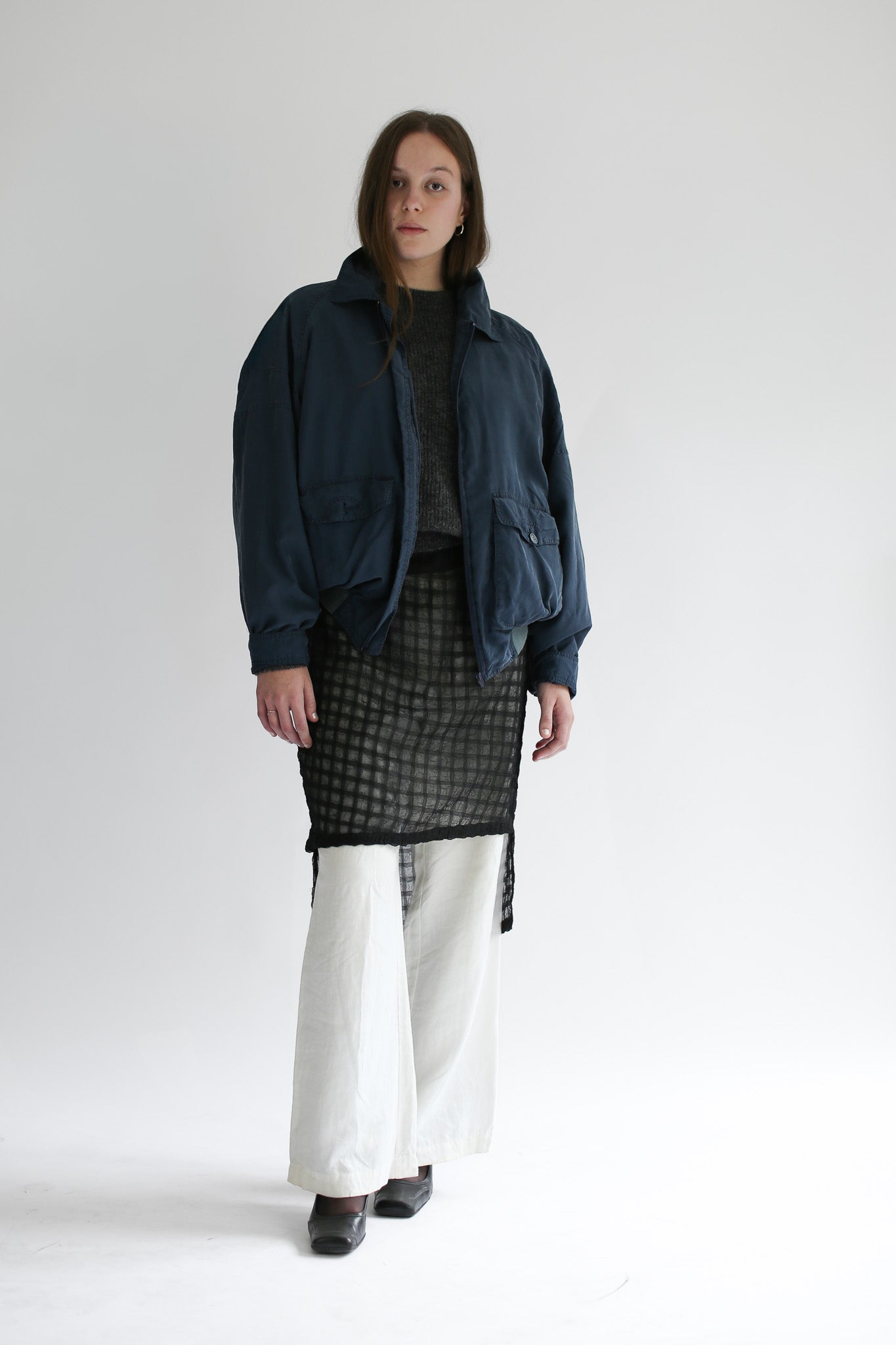 Woman wearing a grey sweater and plaid skirt with a blue bomber on a white background