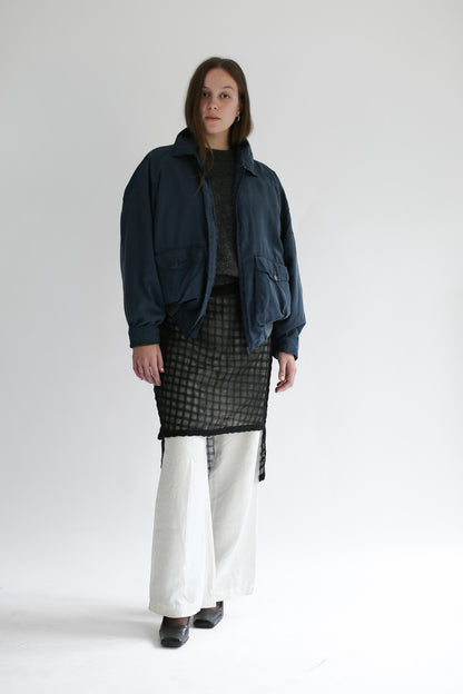 Woman wearing a grey sweater and plaid skirt with a blue bomber on a white background