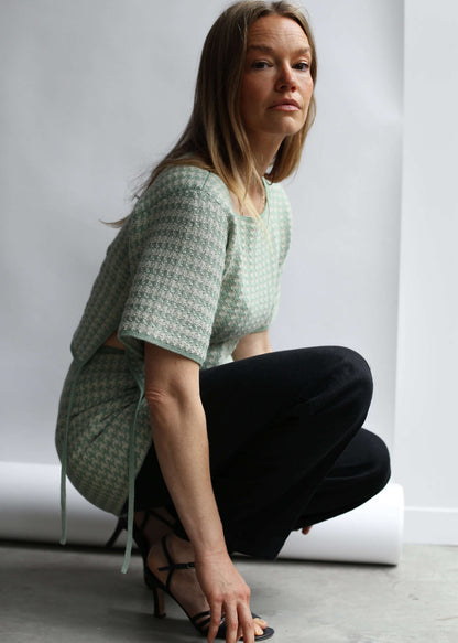 Model croching wearing a green houndstooth knit top and skirt against a white background