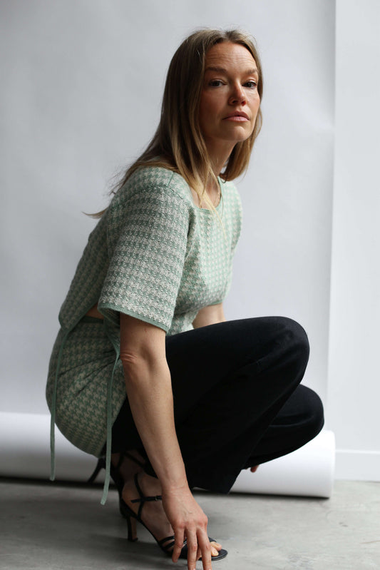Model croching wearing a green houndstooth knit top and skirt against a white background