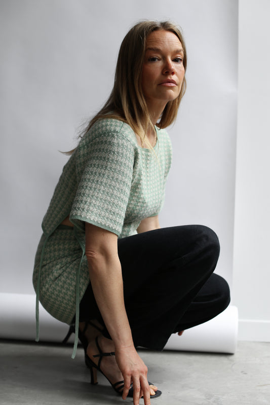 Model croching wearing a green houndstooth knit top and skirt against a white background