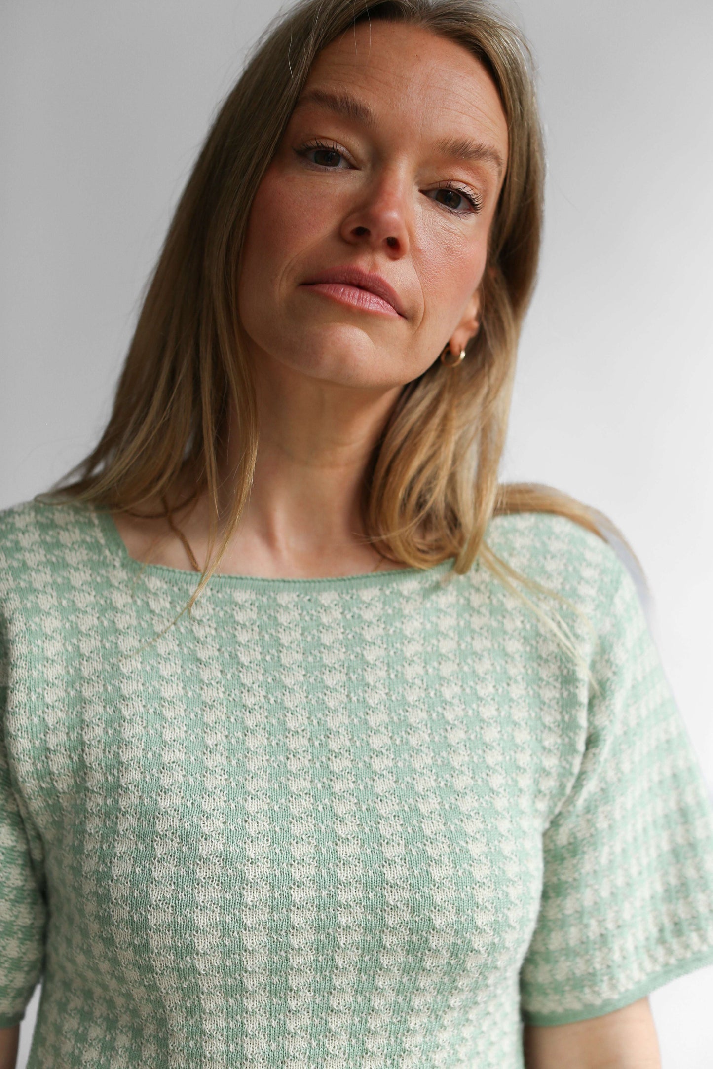 Close-up on a model wearing a green houndstooth knit top and skirt against a white background