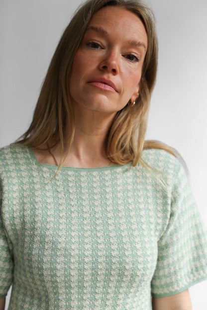 Close-up on a model wearing a green houndstooth knit top and skirt against a white background