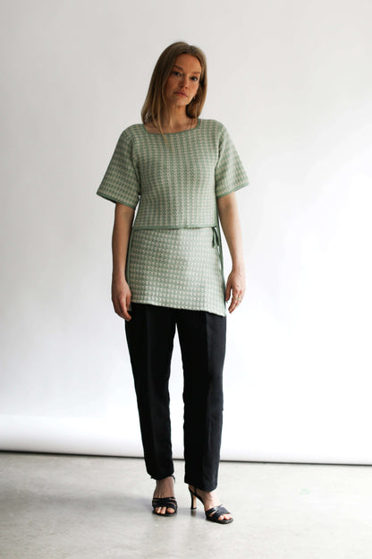 Model standing wearing a green houndstooth knit top and skirt against a white background