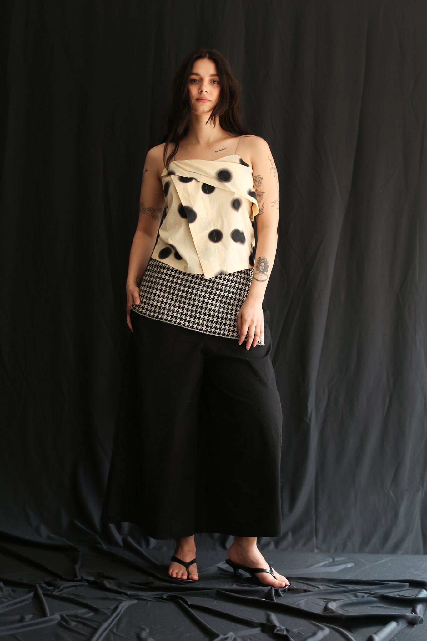 Woman wearing a white polka dot cloth as top and a houndstooth patterned sirt on a black background
