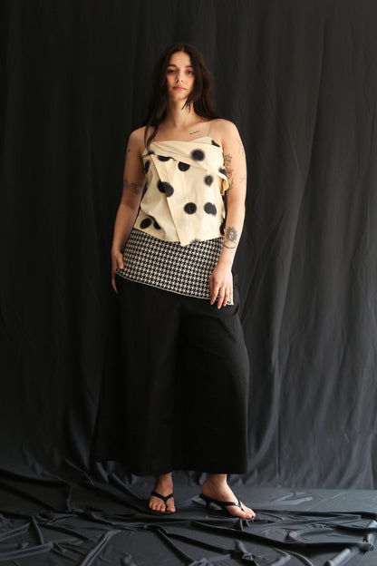 Woman wearing a white polka dot cloth as top and a houndstooth patterned sirt on a black background